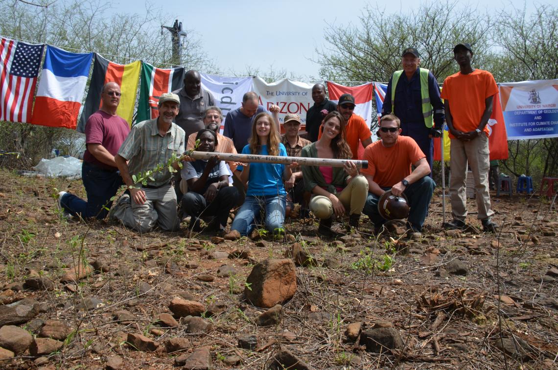 The Hominin Sites and Paleolakes Drilling Project scientific drilling team holds the final core segment collected at the Tugen Hills drill site, from approximately 750 feet below the earth's surface. Flags represent countries and institutions involved in